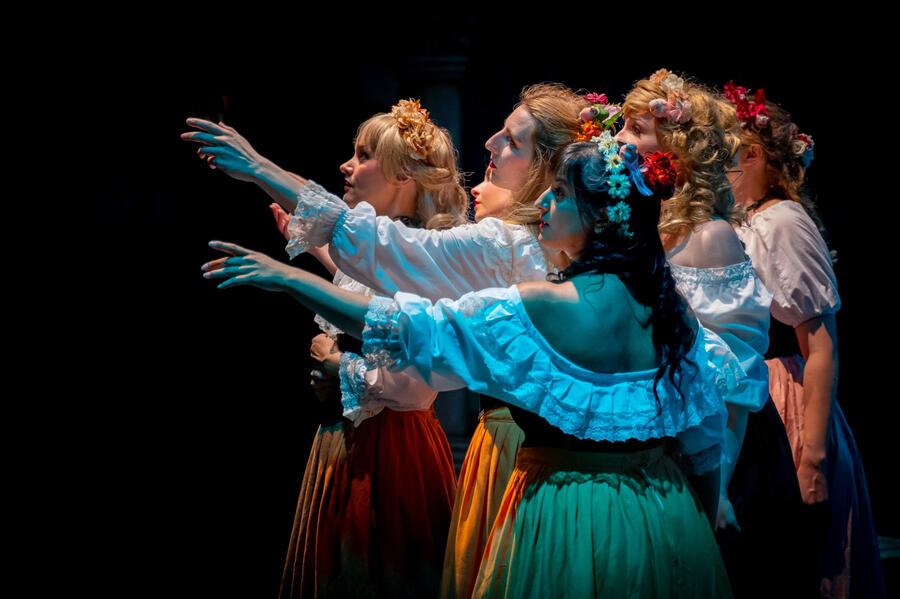 Stage shot of Michelle Kelly and female chorus in period clothes and flowers in their hair