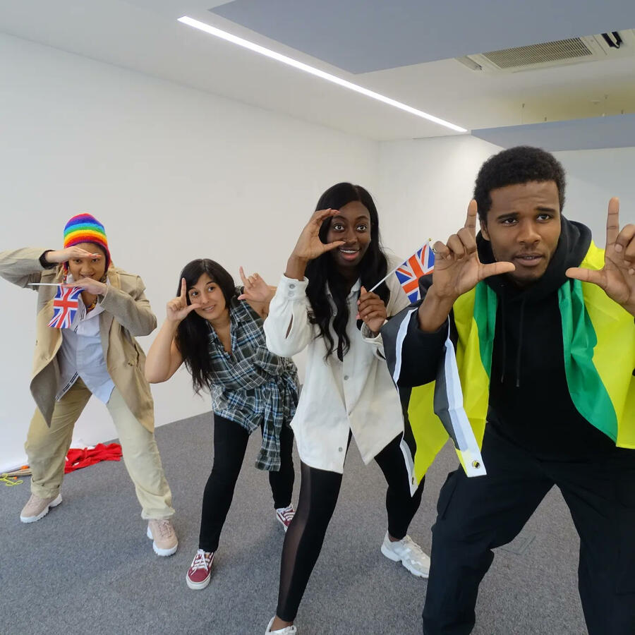 Rehearsal shot of Michelle Kelly miming taking photos with other actors in a crowd